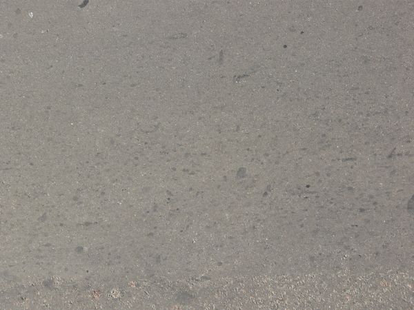 Asphalt texture, light grey in color, with dark stones of various sizes embedded within it. The surface is smooth and rough, with no cracks.